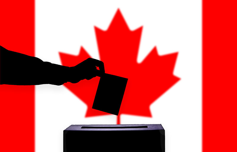 Cadrage sur le bras d’une personne qui dépose un vote dans une urne, le drapeau canadien en fond
