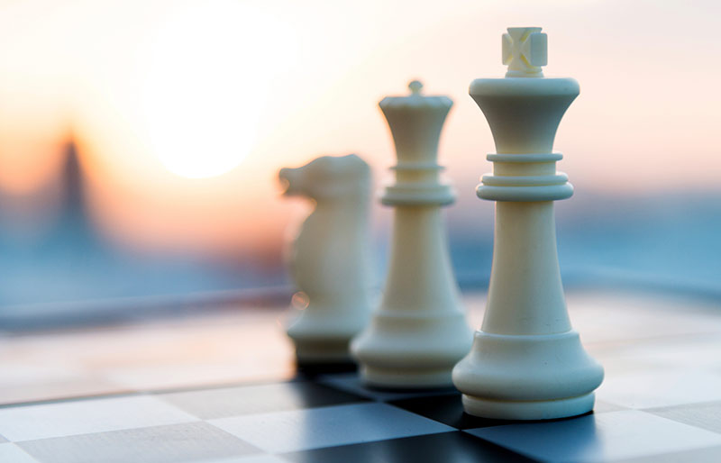 Three white pieces of a chess set on a chessboard, on background sunset.