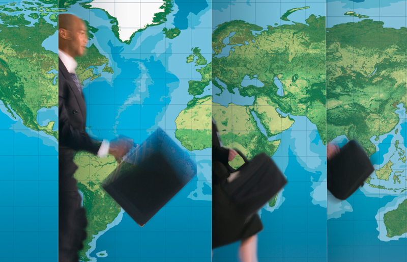 Business person holding a briefcase walking in front of a world map.