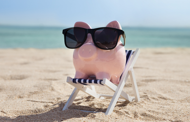piggybank wearing sunglasses, sitting on beach chair on a beach. 
