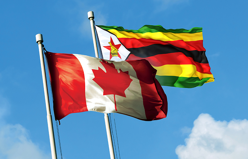 Le drapeau du Zimbabwe et celui du Canada sur un ciel bleu.