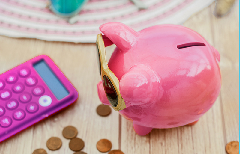 Un cochon tirelire portant des lunettes de soleil est posé sur une table avec de la monnaie et une calculatrice.