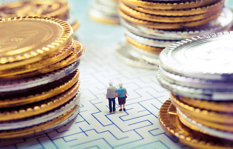 Miniature elderly couple walking over a maze floor pattern between stacks of coins