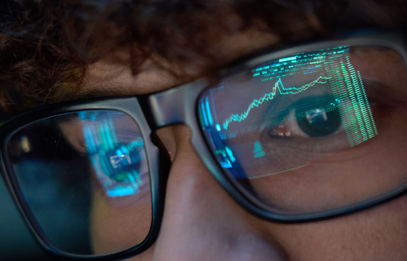 Business graphs reflected in close up of person's eyeglasses.
