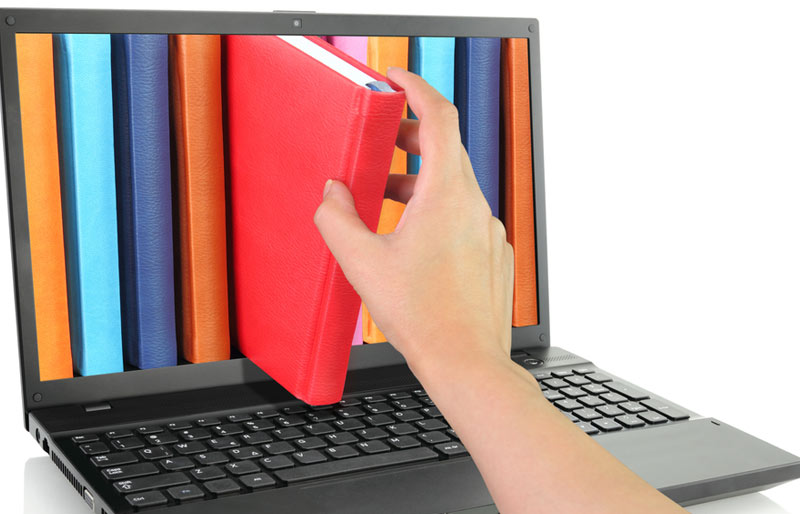 Une main attrape un livre à travers l’écran d’un ordinateur portable.