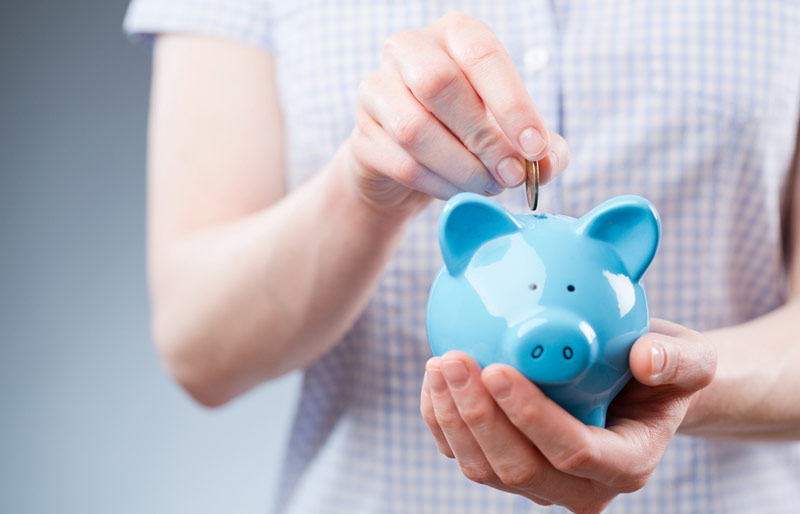 A close-up image of a female in a short sleeved shirt placing a coin into a blue piggy bank.