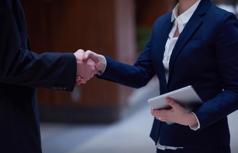 A photograph of a female and male business professional shaking hands. 
