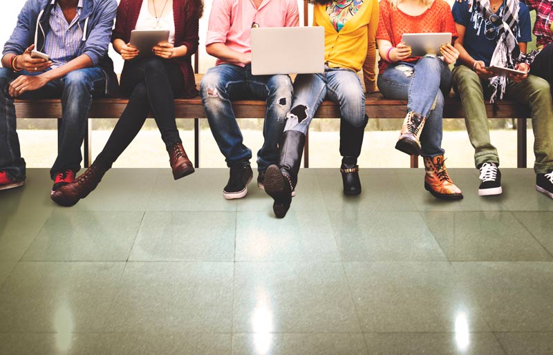 Six jeunes de la génération Y assis sur un banc regardent leurs appareils électroniques.