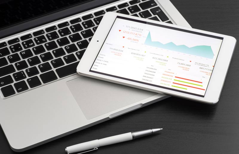 L’intégration de l’analyse de données dans le quotidien des entreprises est illustrée par l’image d’une tablette électronique affichant des données financières, posée sur un ordinateur portable. 