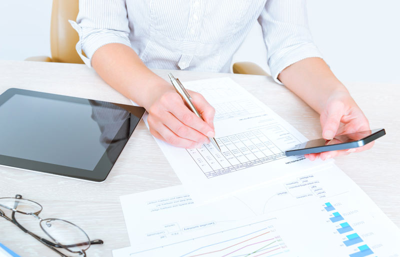 Une professionnelle, calculatrice à la main, effectue des calculs sur un document financier.