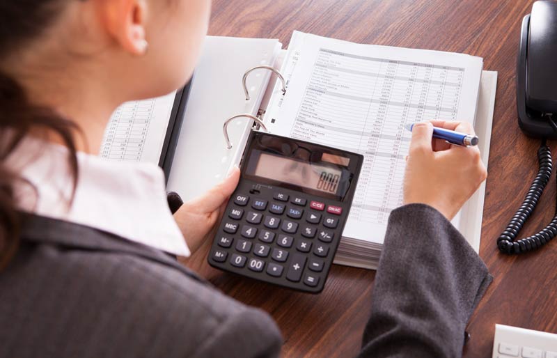 Une comptable utilise une calculatrice pour vérifier des feuilles de données dans un cartable.