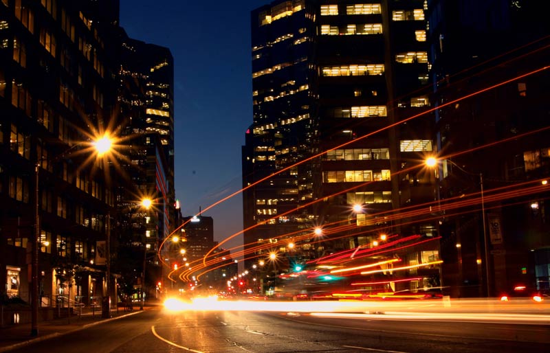 Photo de nuit prise avec une vitesse d’obturation lente, qui montre les traînées de lumière laissées par des phares de voitures dans une ville.