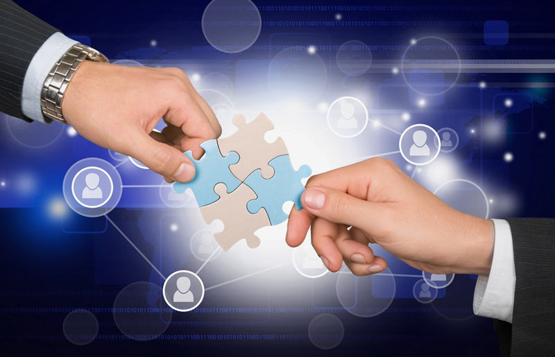 A concept image of two business professionals connecting puzzle pieces with interconnecting people icons. 