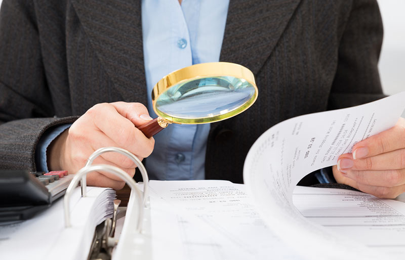 Business person looking at document through magnifying glass.