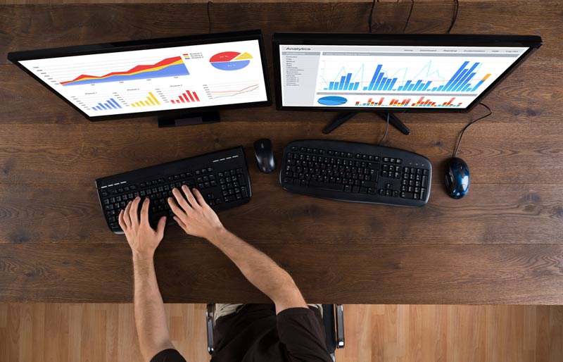 audit data analytics alerts, hand typing in front of two monitors 