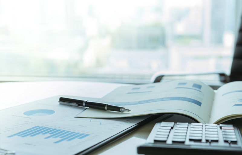 Gros plan sur une calculatrice, un stylo et des rapports financiers ouverts sur un bureau, illustrant le fait qu’il est important d’aider les investisseurs à mieux comprendre l’information d’entreprise.