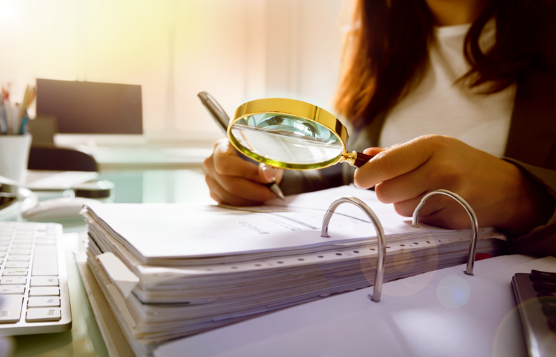 Businesswoman using a magnifying glass to look over a large binder of business documents