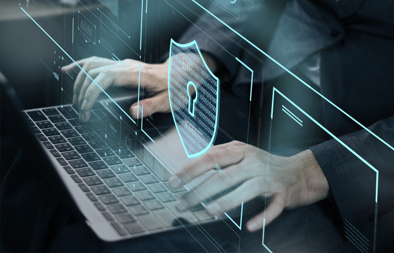 Gros plan sur les mains d'un professionnel qui utilise un clavier d'ordinateur, devant un écran sur lequel se trouve une illustration en lien avec la sécurité, illustrant la gestion des risques liés à la cybersécurité.