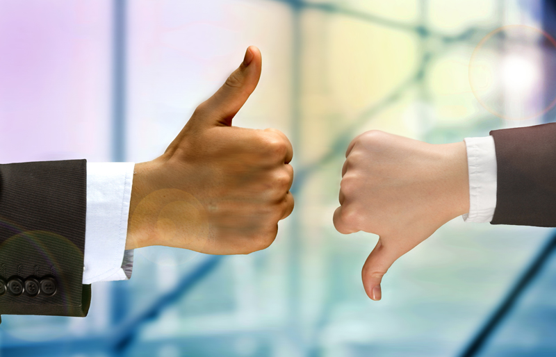The hands of two separate business people, one giving a thumbs down, the other thumbs up
