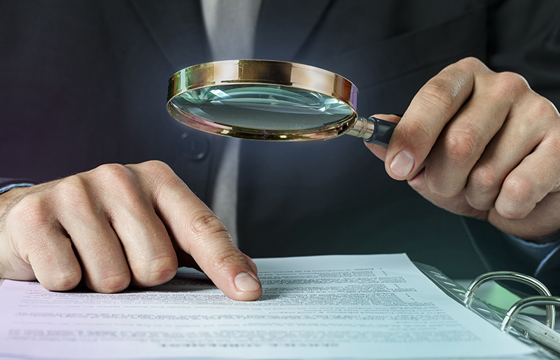 Business person using a magnifying glass to examine business documents