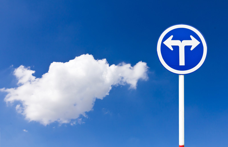 Un panneau de signalisation bleu avec des flèches blanches pointant des directions opposées sur un fond de ciel bleu avec un nuage