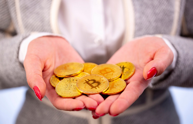 Close up of businessperson's hands holding gold-coloured coins bearing the bitcoin logo.