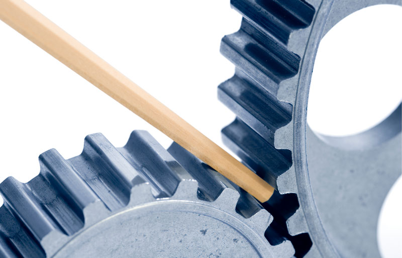 Two interlocking cogwheels with a wooden stick positioned to stop their movement.