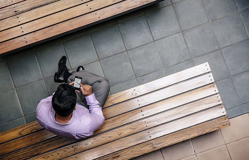 Cadrage vue aérienne d’un professionnel assis sur un banc qui utilise son téléphone portable