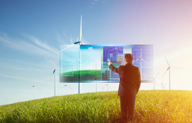 Businessperson using a giant touch screen standing in a field with wind turbines.