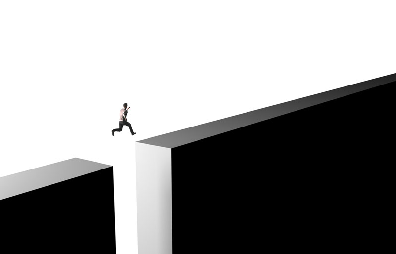 Business person jumping across a gap in a wall.