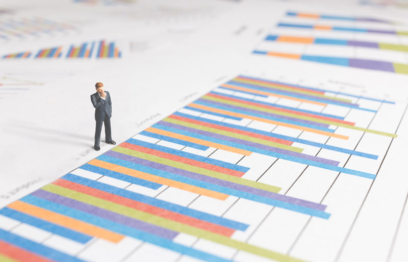 Miniature businessperson stands on a printed bar graph.