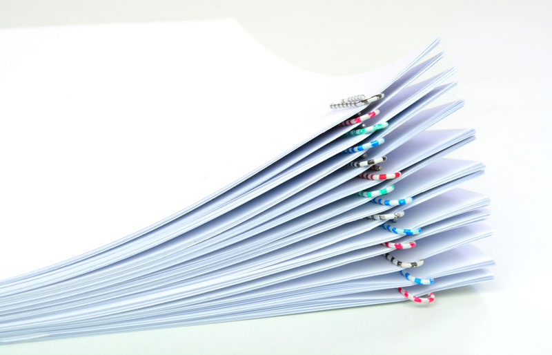 Close up of a stack of white papers held together by colourful paper clips.