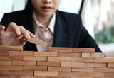 Business person adding a wooden block to a partially completed wall.