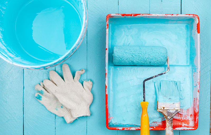 Cadrage sur une main qui tient un rouleau de peinture pour ajouter une couleur bleue à un mur.