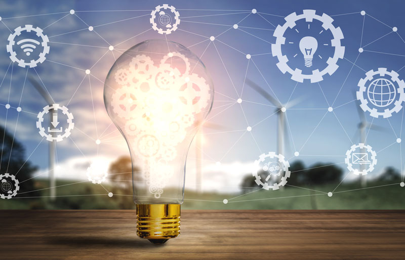 Illuminated lightbulb on wooden surface, green field in background, superimposed quality and productivity icons.