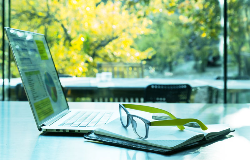 Open laptop and glasses, wooded scenery in background.