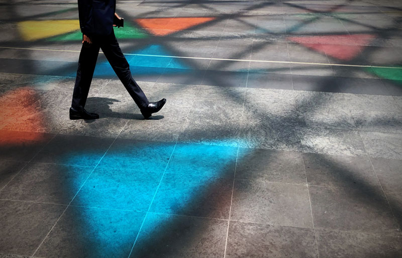 Image d’un professionnel qui marche sur un pavé en ciment reflétant un ombrage de motifs triangulaires et de couleurs