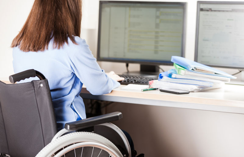 Businessperson seated in a wheelchair works at a computer.