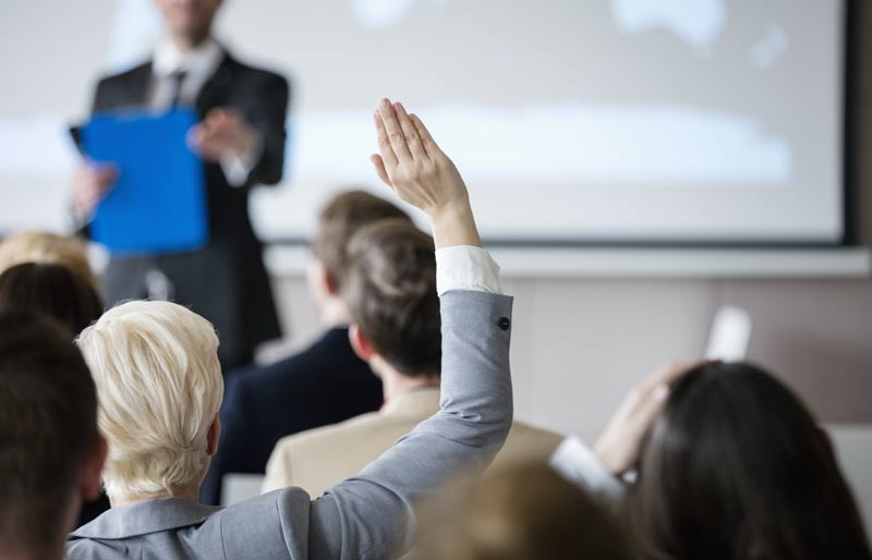 Une femme qui assiste à un séminaire lève la main pour poser une question.