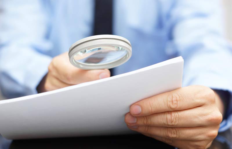 Male accountant looking at a file through a magnifying  glass.