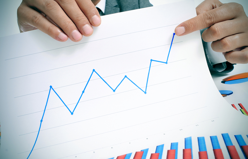A close-up image of a male business professional holding up a line graph and pointing to the upturn in revenue. 