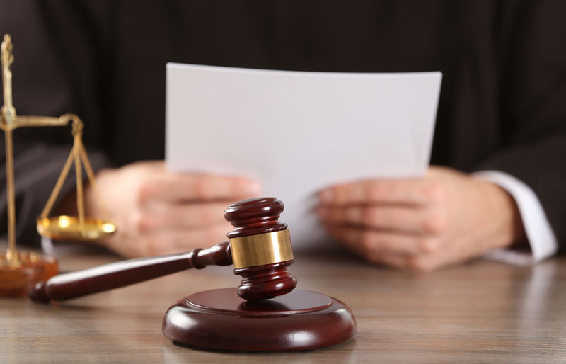 A close-up of a business professional at a desk reading a report and on the desk there is a gavel and The Scales of Justice. 