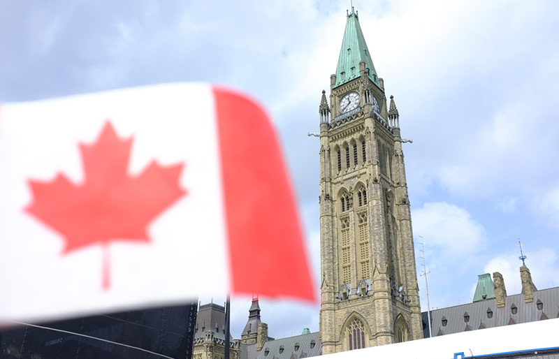 Gros plan sur un drapeau canadien devant les édifices du Parlement.