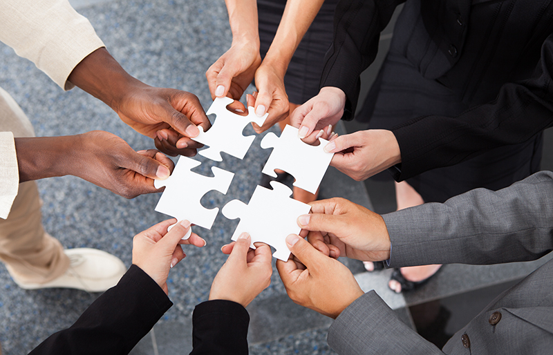 Hands of several business people each holding a puzzle piece to make one large piece