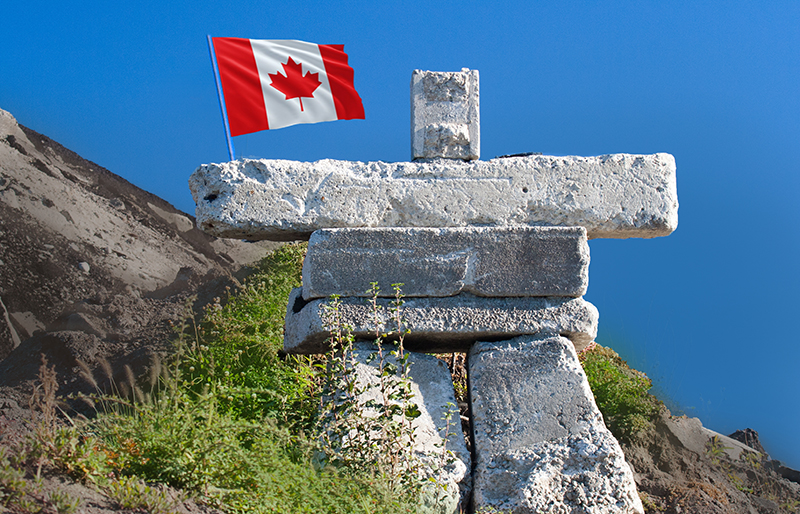 Un inukshuk de pierres grises qui semble tenir un drapeau canadien dans décor paysage du Nord canadien.