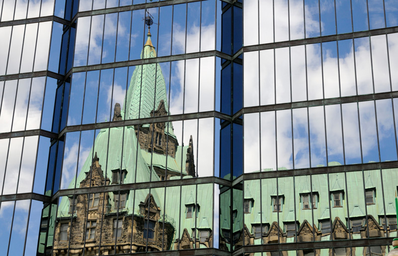 Image of Canada's Parliament buildings reflected in windows of nearby building.