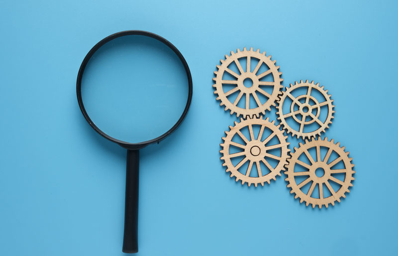 Top view of magnifying glass and gears on blue background.