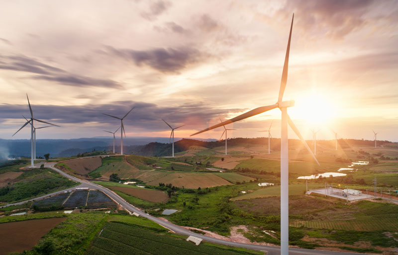 Panoramic view of a valley at sunset with wind turbines.