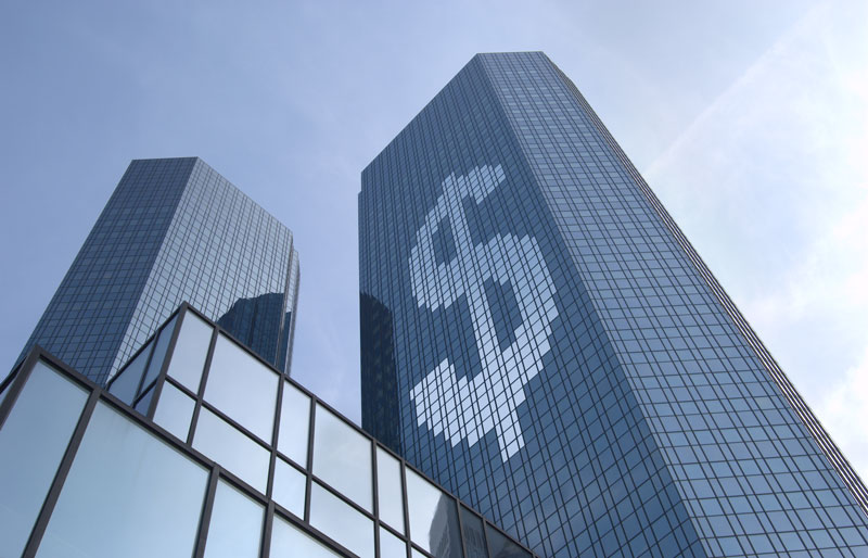 View looking up at three office towers, one with the pattern of a large dollar sign in its windows.
