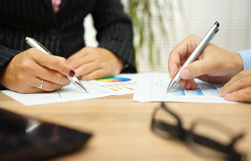 A close-up image of a female and male business professional at a table reviewing various reports.